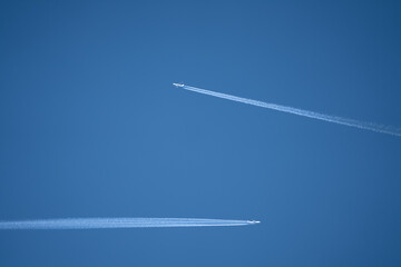 a pair of twin engined jet liner aircraft with contrails, passing at high altitude, clear blue sky