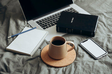 Bible, phone, laptop and cup of coffee on a grey bed background. studying Bible.