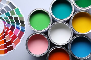Cans of bright paints and color palettes on grey background, flat lay