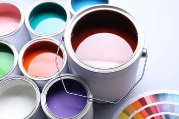 Cans of bright paints and color palettes on light background, closeup