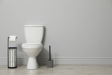 Ceramic toilet bowl, brush and paper near grey wall indoors. Space for text