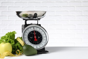 Mechanical kitchen scale with bowl of products and measuring tape on white wooden table against...