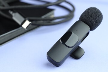 Lavalier microphone, cord and notebook on light blue background, closeup