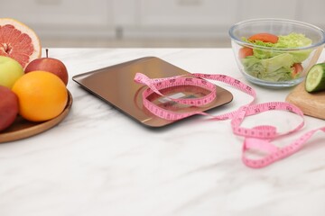 Kitchen scales, measuring tape, salad and fruits on white table indoors, closeup