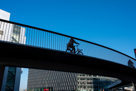 Silhouetted bike rider on curved bridge between buildings in Copenhagen, Denmark, symbolizing healthy transport, clean air and integrated urban cycling infrastructure.