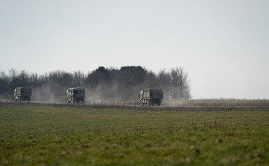 a convoy of British army MAN SV 4x4 utility trucks on a dusty track