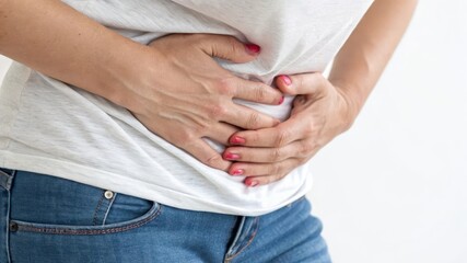 A woman clutches her abdomen, indicating discomfort or pain, while wearing casual attire, suggesting a moment of distress or health concern.