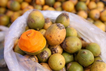 Tucumã, uma fruta tropical nativa da região amazônica, incluindo Manaus, Brasil. As frutas estão aglomeradas, com uma porção delas dentro de um saco plástico transparente aberto, que está parcialmente