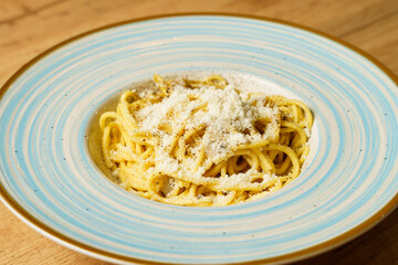 Classic spaghetti cacio e pepe with grated cheese on a blue-striped plate