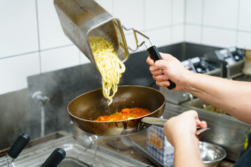 Fresh pasta being added to a pan with tomato sauce