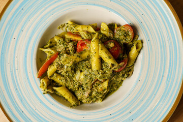 Pasta with creamy pesto sauce and cherry tomatoes on a blue-striped plate