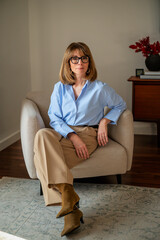 Obraz premium Portrait of smiling blond haired woman sitting in an armchair in her cozy home