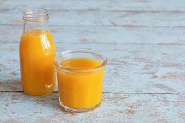 Fresh mango juice in a glass glass with mango slice on blue wooden background. Exotic drink, Trending colors.