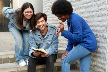 Three multicultural friends enjoying a book together outside, displaying joy and camaraderie