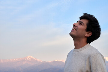 Cheerful man in sweater looking joyfully skyward with snowy mountains in the background