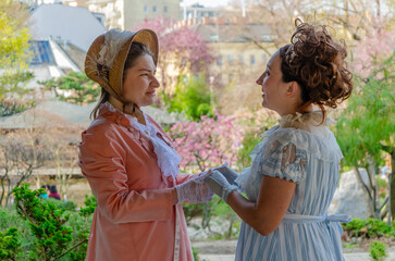 Fototapeta premium A 19th century style female friendship - whispering and chatting amongst the flowering trees.