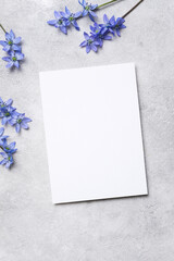 Vertical blank card mockup surrounded by soft blue spring flowers on a light concrete background, top view flat lay perfect for elegant wedding or seasonal invitations