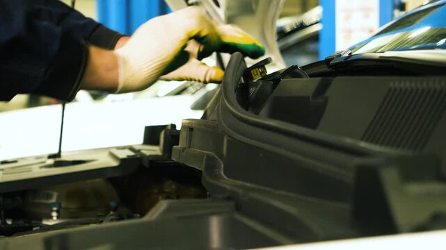 Professional auto mechanic disassembling components under the hood to access and replace the windshield wiper mechanism. Concept of vehicle maintenance, repair, and automotive service