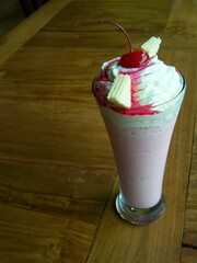 Delicious pink milkshake with whipped cream, cherries, and wafers in a glass.