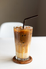 Iced of coffee cup with tube sucking on glass cup on white table. Vertical photo
