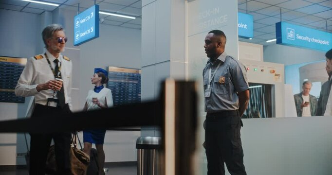Flight Crew in Airport Terminal: Professional Airline Captain, Two Beautiful Stewardesses in Uniforms Walking with Suitcases for Flight, Passing by African American TSA Officer at Security Checkpoint