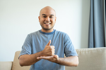 Portrait view of happy young deaf asian man showing sign language and looking at camera at home, a...