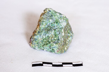 A pistachio green Epidote rock sample with trace of red garnet with a 5cm scale on a white...