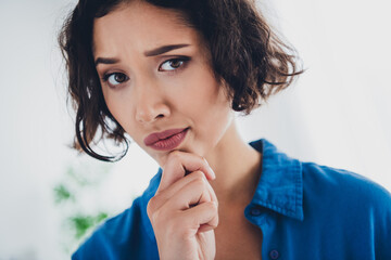 Young woman indoors wearing a blue shirt while exhibiting a thoughtful expression in a bright home...