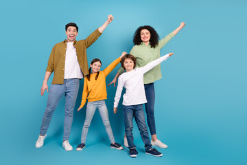 Fototapeta premium Happy family of four posing together against a blue background, showing gestures of joy and unity, embracing lifestyle and leisure