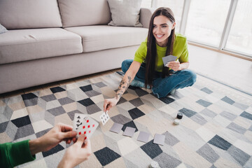 Smiling young woman playing cards on a patterned rug in a bright, cozy living room on a relaxed...
