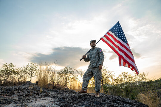 Hand Waving the Flag of the United States of America in memorial day . Us soldier holding American flag celebrating.US Army soldier celebrates holding USA flag celebrating Independence USA day - Powered by Adobe