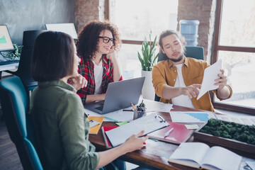 Young diverse coworkers collaborating in a modern workspace, sharing ideas and papers, showcasing teamwork