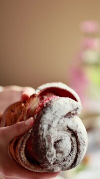 A woman breaks cruffin, showing a fluffy, tender dough with a berry filling. cruffin with raspberry jam. Easter bread. Easter eggs and spring flowers