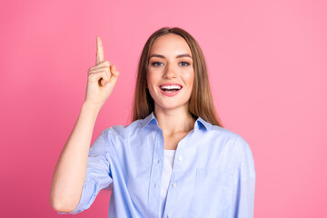 Young Woman Smiling and Pointing Upward on a Pink Background, Wearing a Blue Casual Shirt,...