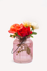 Colored roses in a pink glass vase with water on a white background with copy space