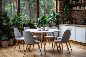 Fototapeta premium Modern dining room with round white table, grey chairs, and Scandinavian-style design. Light wooden accents, white cabinets, and potted plants creating a cozy atmosphere with natural light.