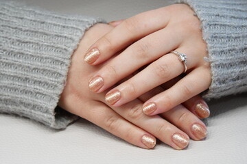 Woman's hands with gold glitter manicure and a diamond ring