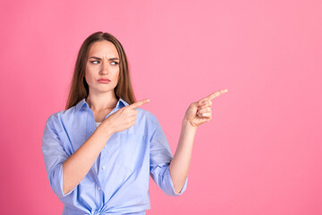 Young woman in casual blue shirt making a surprised facial expression and pointing fingers on a...