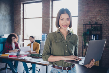 Young confident professional using a laptop in a relaxed modern coworking office with colleagues...