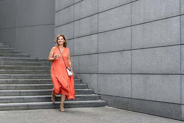 Middle-aged woman walking down concrete stairs against background of concrete slabs in city on summer day