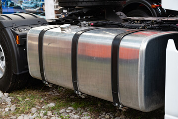 Close-up of a truck fuel tank with straps on a grassy and rocky ground.