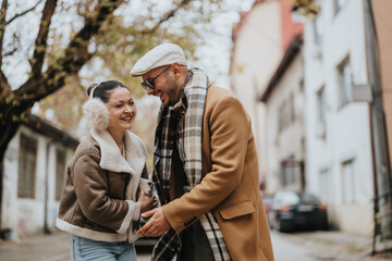 A happy couple shares laughter outdoors in an urban setting. The man and woman, dressed warmly, exude joy and connection while surrounded by trees and buildings in a charming city environment.