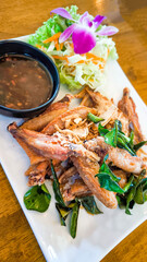 Fried chicken wings in a white plate on a wooden table decorated with orchids.