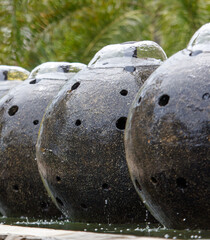 A row of black vases with holes in them are sitting in a pool of water