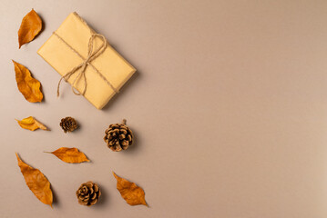 Gift box with autumn leaves and cones on beige background. Top view, copy space