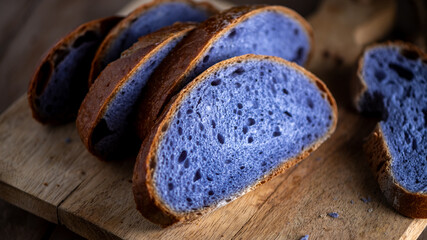 Slices of freshly baked purple bread cooked in blue Thai ancha tea sit on a rustic wooden cutting...