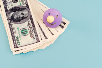 Dollar bills and a baby pacifier on an isolated blue background. A place for the text, the concept...