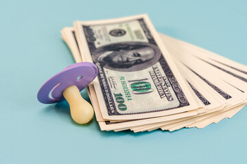 Dollar bills and a baby pacifier on an isolated blue background. A place for the text, the concept of expenses for children's needs and purchases.