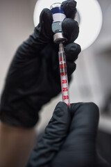 Fototapeta premium Hands in black gloves holding syringe and vial, precise medical procedure equipment, healthcare concept