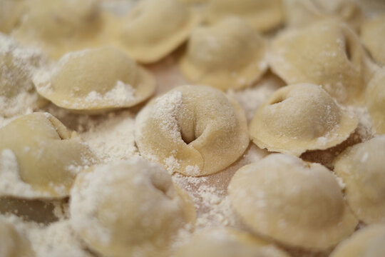 Close-up of traditional homemade dumplings sprinkled with flour, arranged on a kitchen surface ready for cooking.